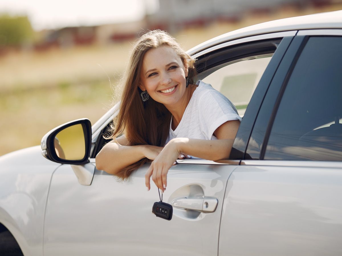 A happy car buyer leaning out of her new car holding the keys